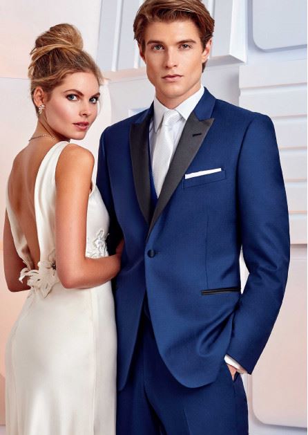 Female model wearing low back wedding gown and male model wearing a blue tuxedo