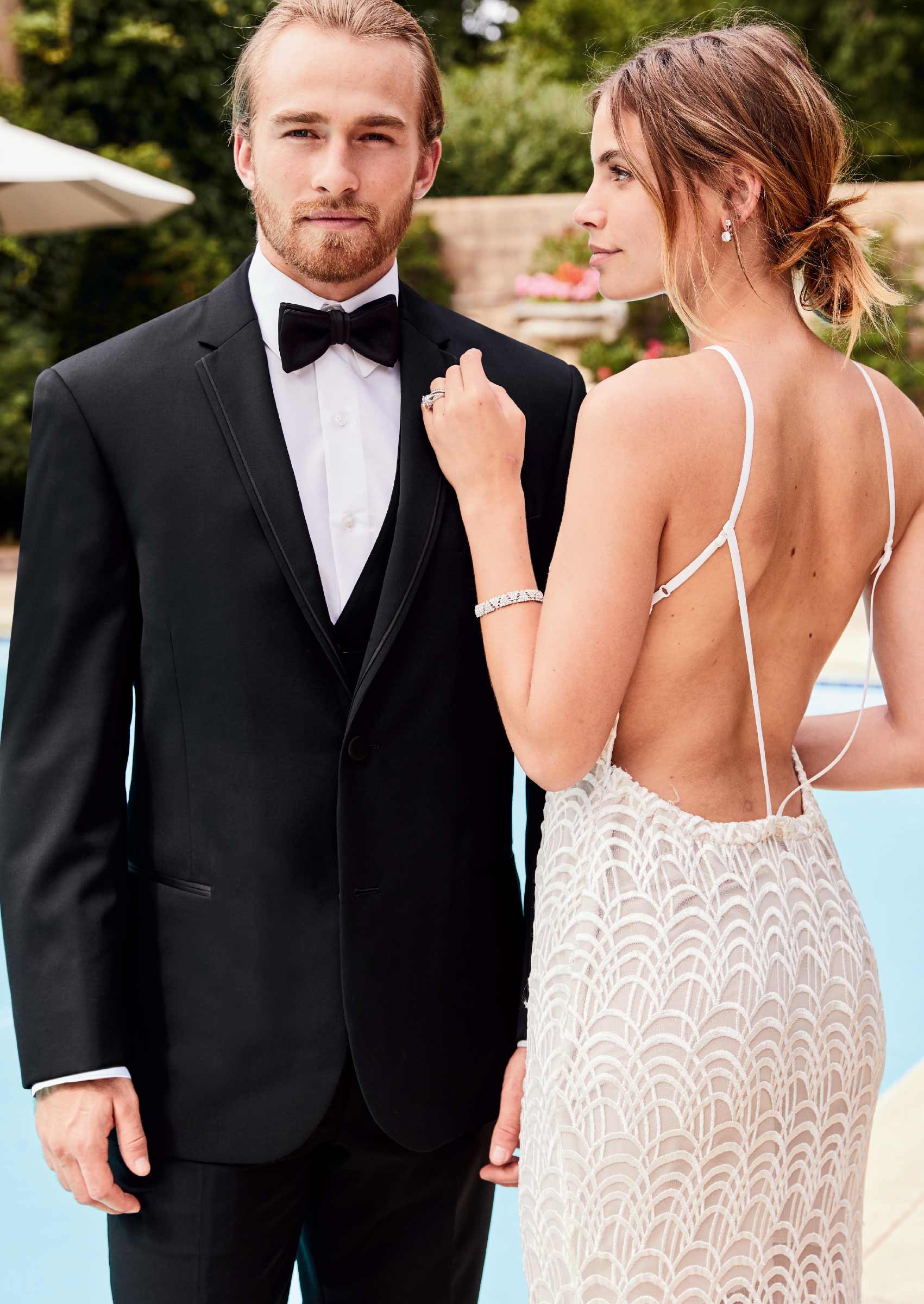 Male model wearing a black tuxedo with bowtie and female model wearing backless evening gown